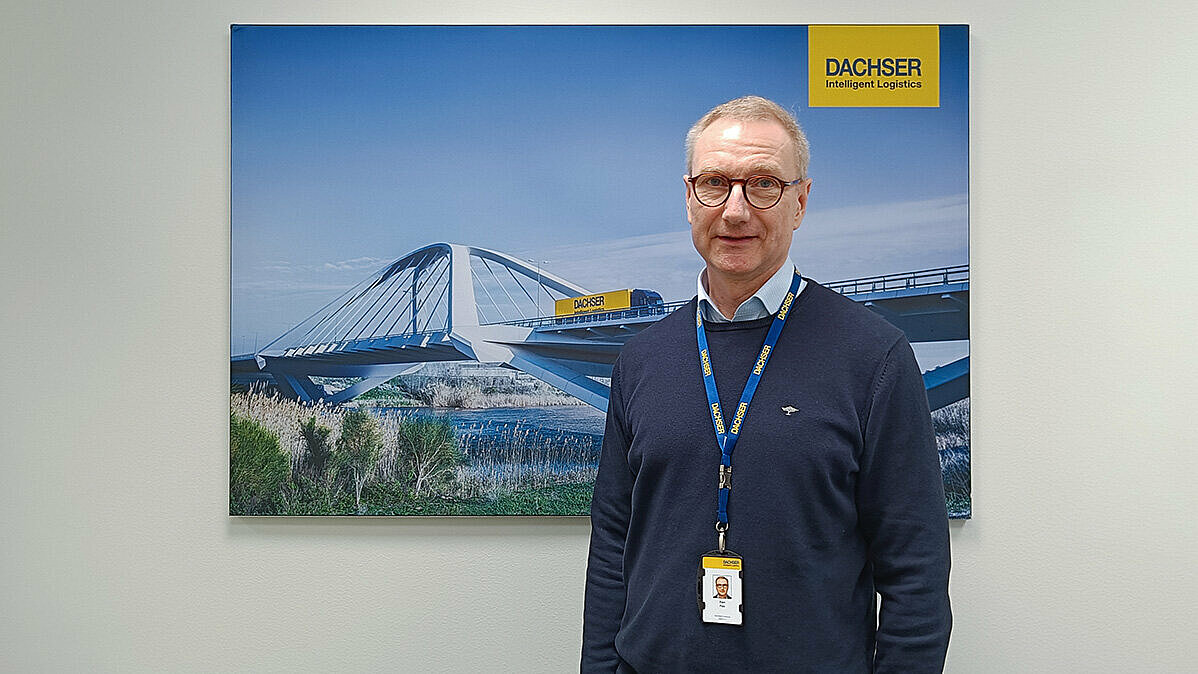 Mies tummansinisissä vaatteissa seisoo Dachser-julisteen edessä