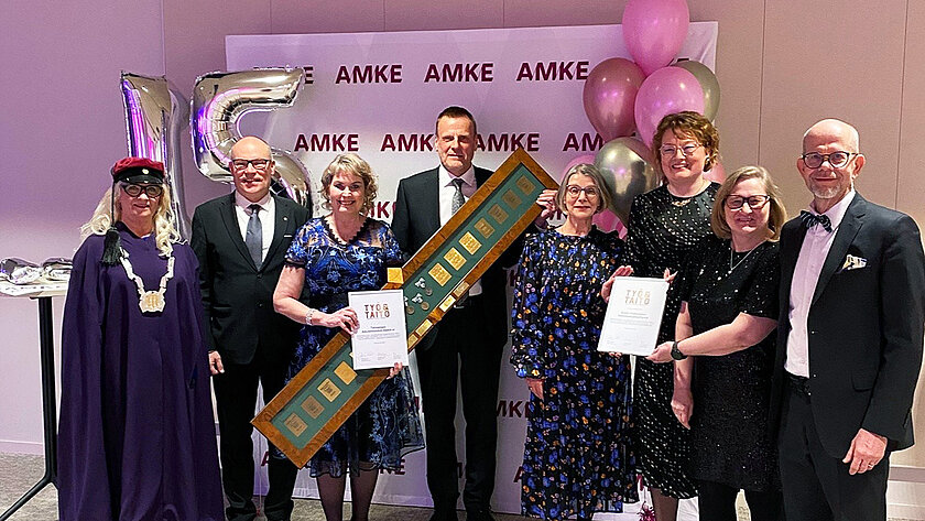 Joukko ihmisiä juhlapuvuissa ilmapallojen alla kunniakirjan ja palkintojen kanssa.