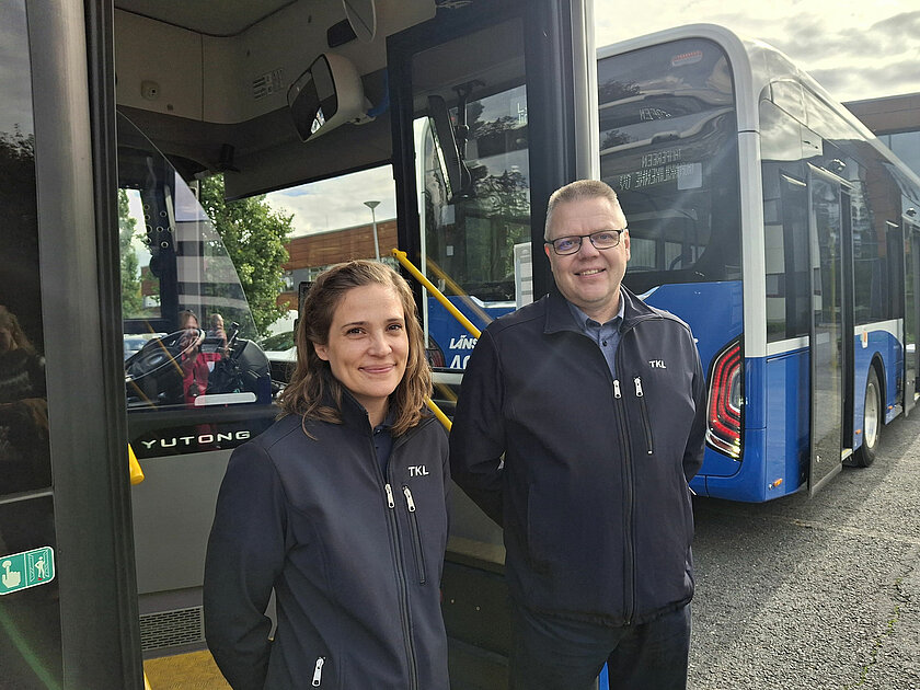 Nastasia ja Tommi poseeraavat bussin edustalla, bussissa etuovet auki. 