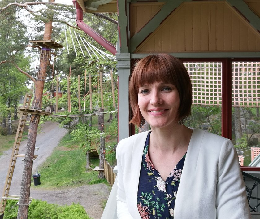 Nainen seisoo hymyillen valkoisessa jakussa.