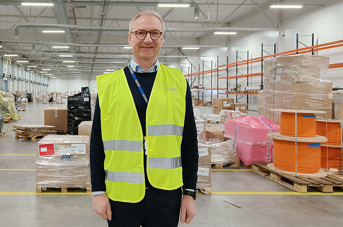 Mies seisoo valoisassa varastohallissa turvaliivi päällään.