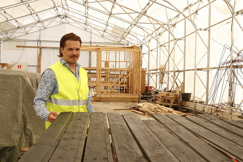 Jussi huomioliivi päällään opiskelijoiden harjoittelutilassa, lautapinoja taustalla.
