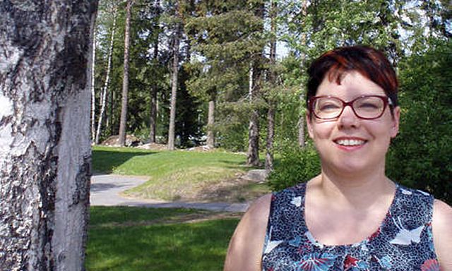 Johanna Vierula seisoo puistossa, puiden lähellä..