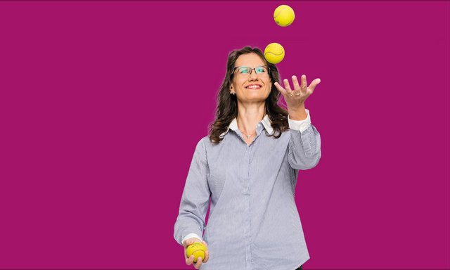 Kauluspaitainen nainen jonglööraa kolmella tennispallolla.