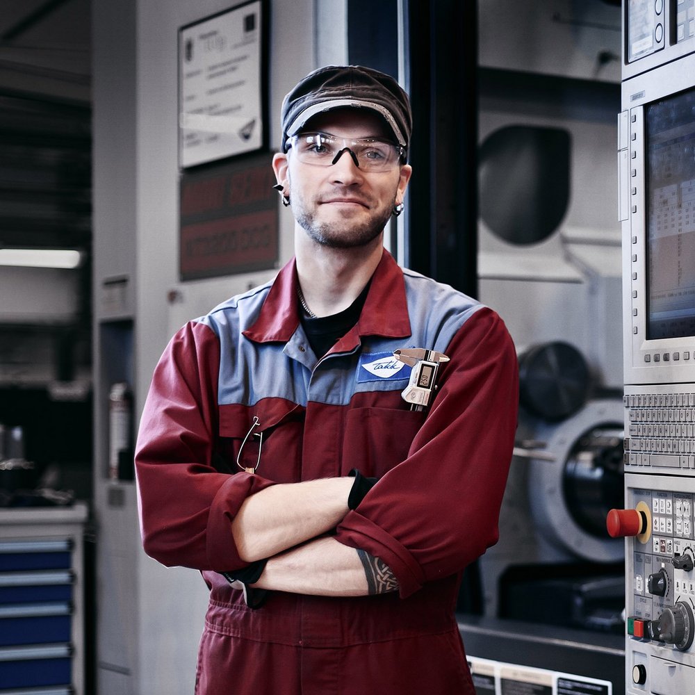 Mies työvaatteissa seisoo CNC-koneen edessä.