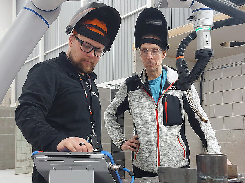Kaksi kouluttajaa hitsauscobotin äärellä valmistelemassa hitsausta.
