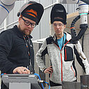 Kaksi kouluttajaa hitsauscobotin äärellä valmistelemassa hitsausta.