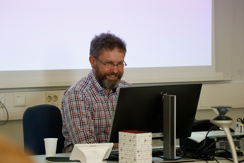 Tapio Halla istuu luentopöydän ääressä, tietokoneen takana. 