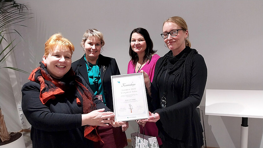 Neljä henkilöä pitelee kunniakirjaa.