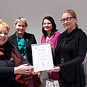 Neljä henkilöä pitelee kunniakirjaa.