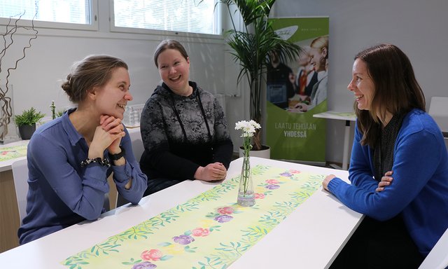 Kolme naista keskustelee pöydän ääressä.