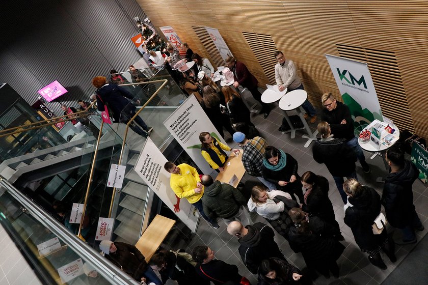 TAKKin infon alakerrassa ihmiset juttelevat työnantajien esittelypisteillä. Nurkassa joulukuusi.