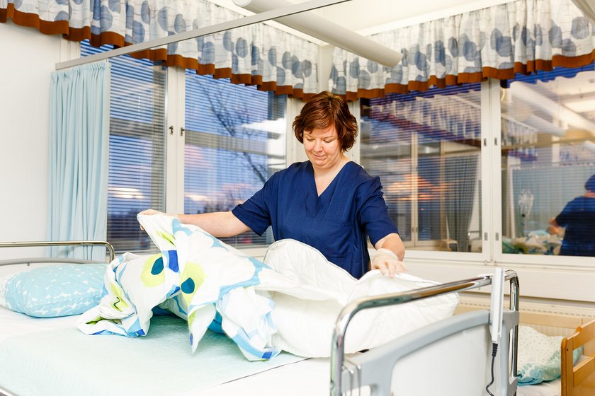 Lähihoitajan työvaatteisiin pukeutunut henkilö vaihtaa lakanoita sairaalasängystä.