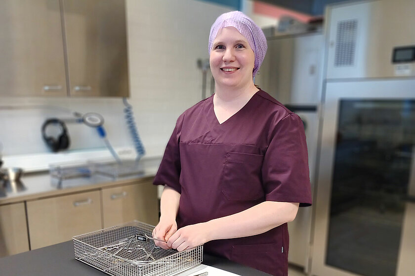 Purppurassa työasussa oleva Karita asettelee välineitä metallikoriin.