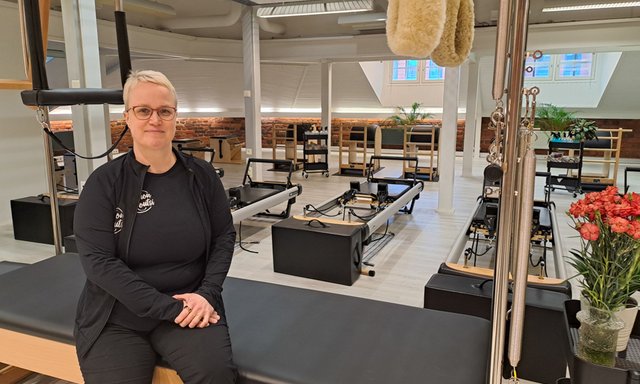 Nainen istuu hymyillen laitepilateslaitteiden edustalla.