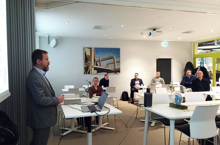 Janne Kerttula pitää puhetta puhujapöydän takaa. Osallistujat kuuntelevat valkoisten pöytien ääressä.