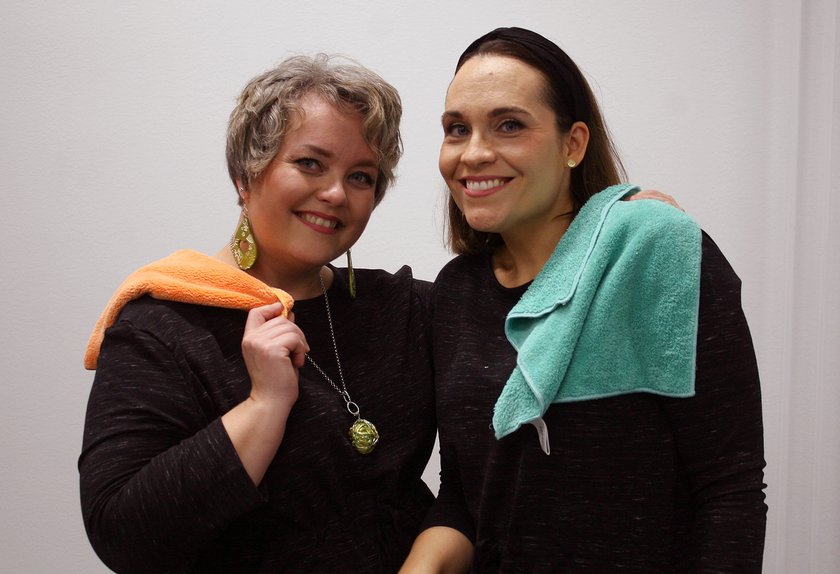 Kaksi naista hymyilee värikkäät siivousliinat hartioilla.