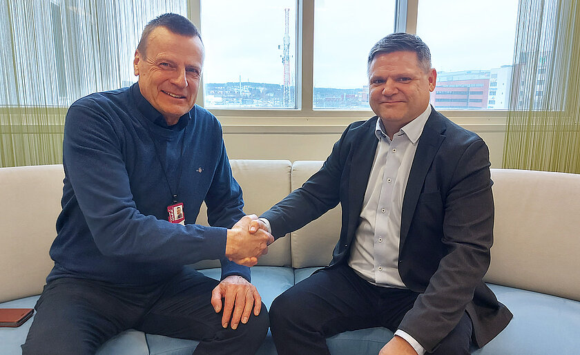 Rehtorit Teppo Tapani ja Jarno Tuimala istuvat suuren ikkunan edustalla sohvalla ja kättelevät.