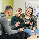 Kolme opiskelijaa istuu sohvalla, yhdellä puhelin kädessä ja näyttää sitä muille. 