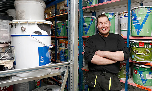 Sisustusalan opiskelija Janne nojaa hyllyyn, jossa maalipurkkeja.