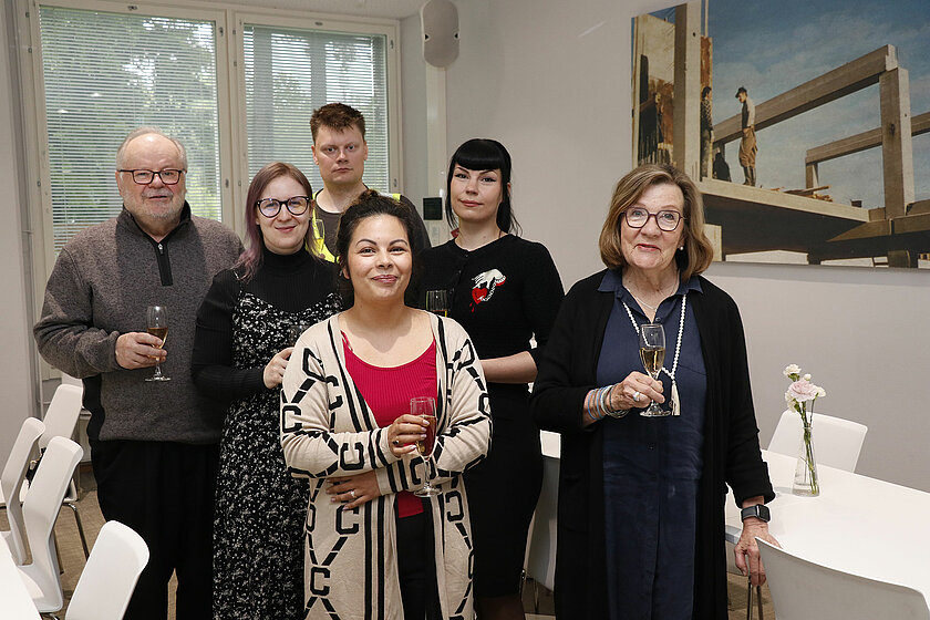 Kuusi henkilöä ryhmänä Nirvan kampuksen ravintolakabinetissa, kuohuviinilasit kädessä. 