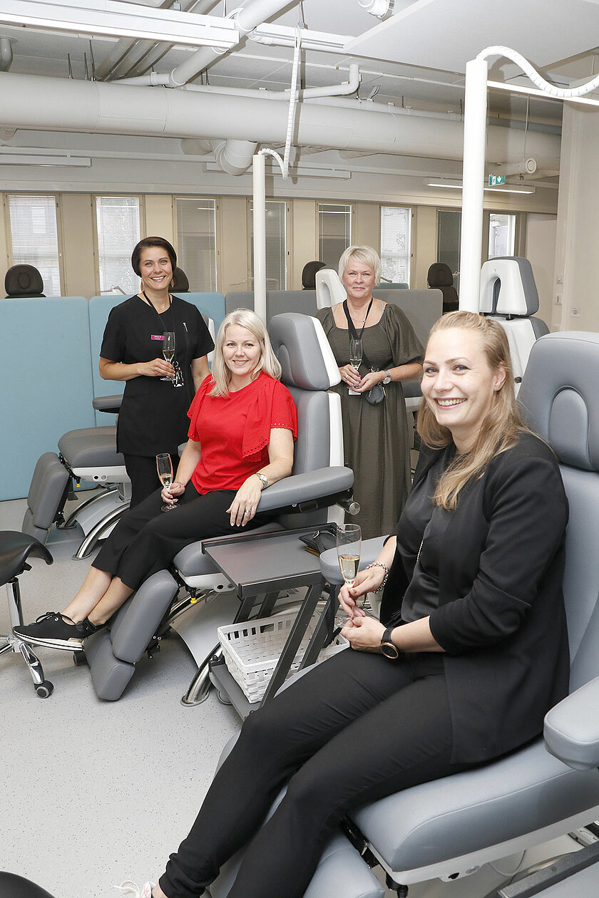 Kaksi henkilöä istuu iloisina jalkahoitotuoleissa, taustalla Lumovan väkeä. 