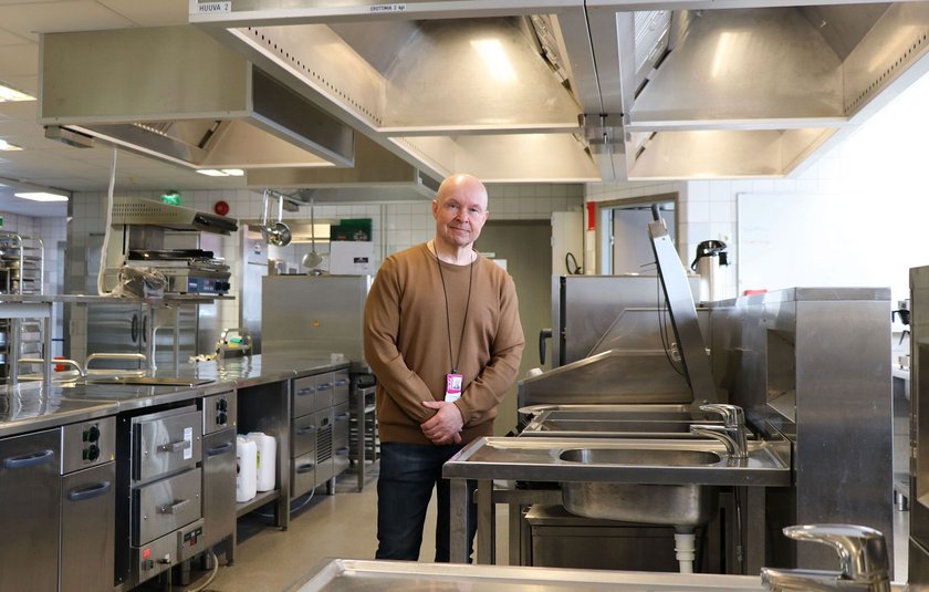 Tapio seisoo keskellä opetuskeittiötä, kirkkaiden valojen alla. 