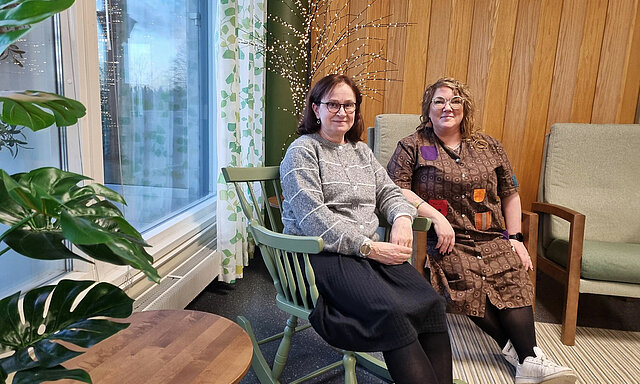 Kaksi naista istuu olohuonemaisessa tilassa.