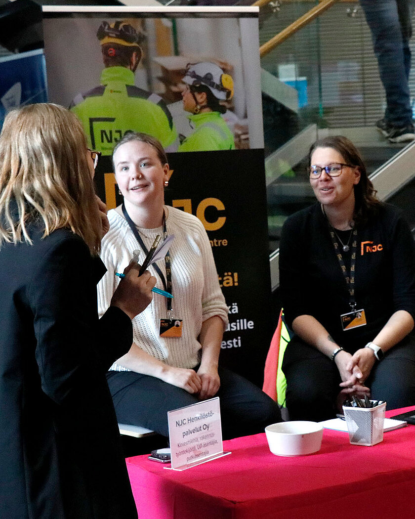 Punaliinaisen pöydän ympärillä käydään keskusteluja.