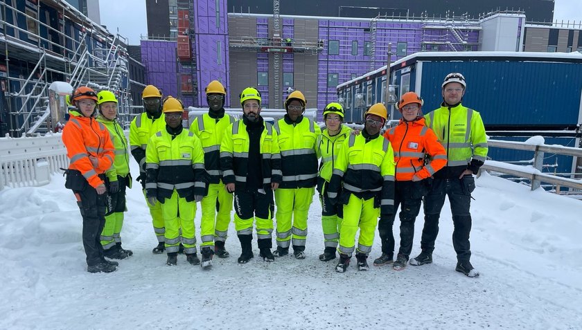 Ryhmä työvaatteissa seisomassa teollisuuslaitoksen edustalla.