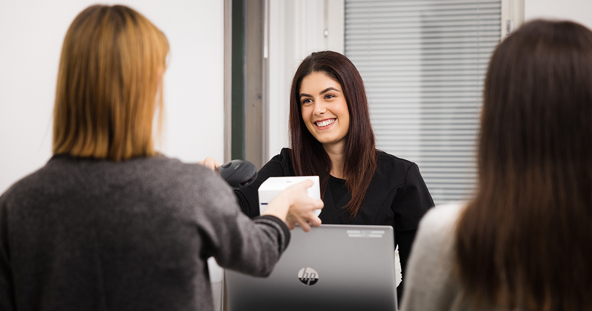 Kaksi asiakasta ja myyjä asiakaspalvelutilanteessa kassalla.