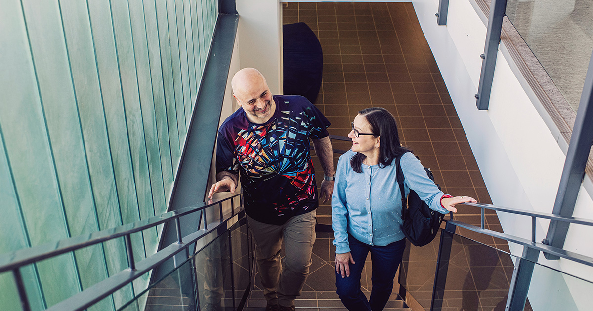 Kaksi ihmistä nousemassa portaita keskustellen yhdessä.