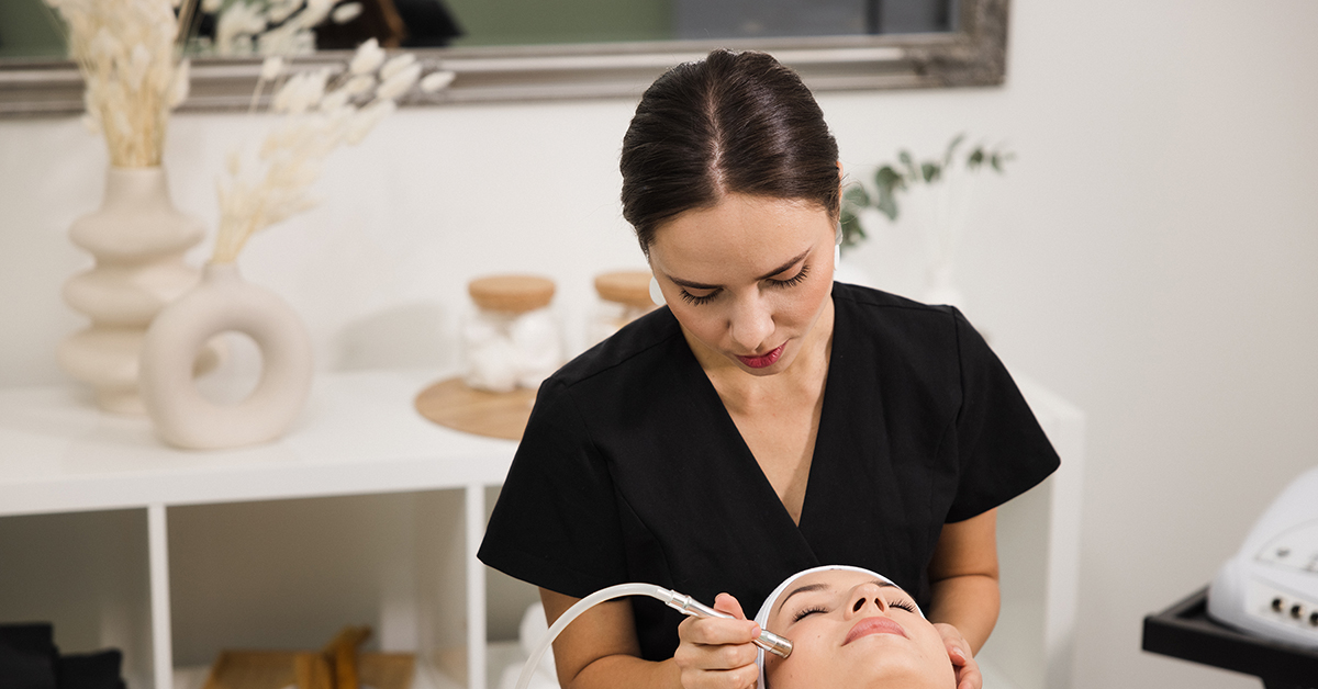Kosmetologi tekee asiakkaalle laitehoitoa kasvoille.