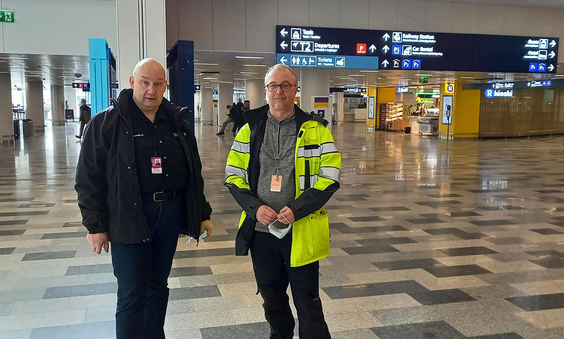 Heikki ja Timo Helsinki-Vantaan lentoasemalla. Timolla yllään huomioväreissä olevat työvaatteet.