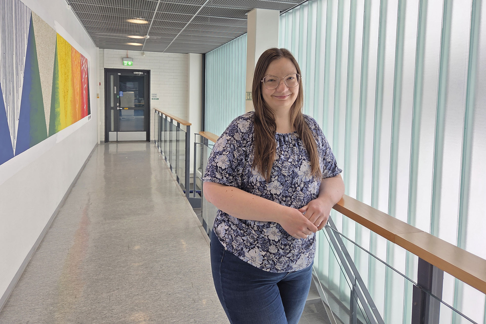 Merkonomiopinnot opiskellut Satu Viherlampi seisoo Tampereen Aikuiskoulutuskeskuksen käytävällä ja nojaa kaiteeseen, takana isot maitolasi-ikkunat.
