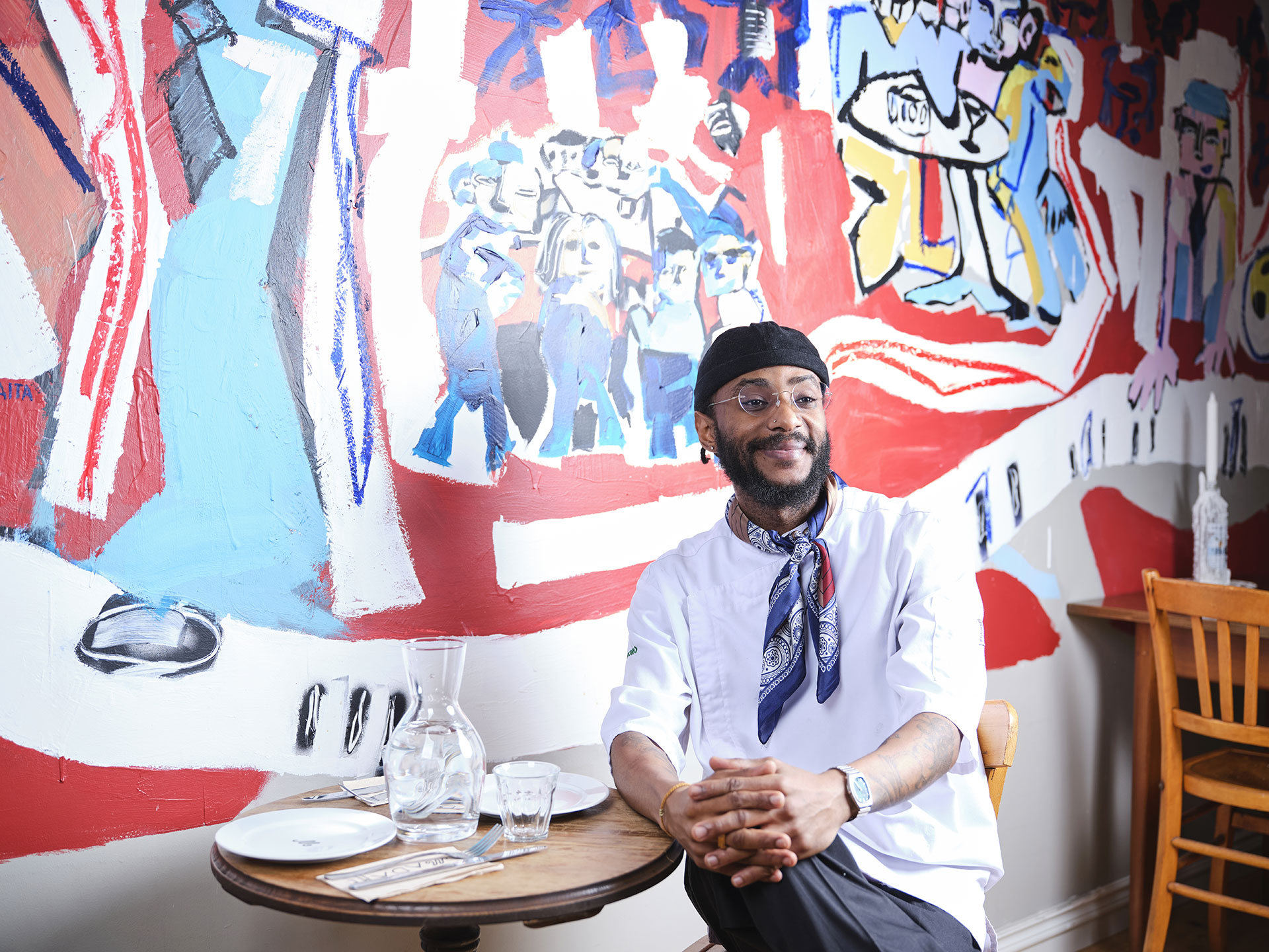 Ravintola-alan opiskelija Jackson istuu ravintolapöydän ääressä, taustallaan seinään maalattu värikäs taidetos.