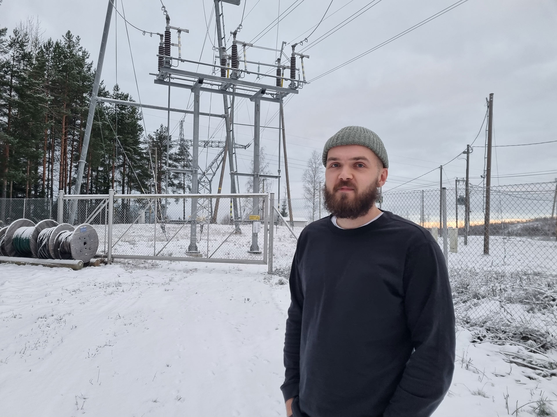 Lauri seisoo talvisessa maisemassa, verkkoaidan takana TAKKin sähkökenttä.