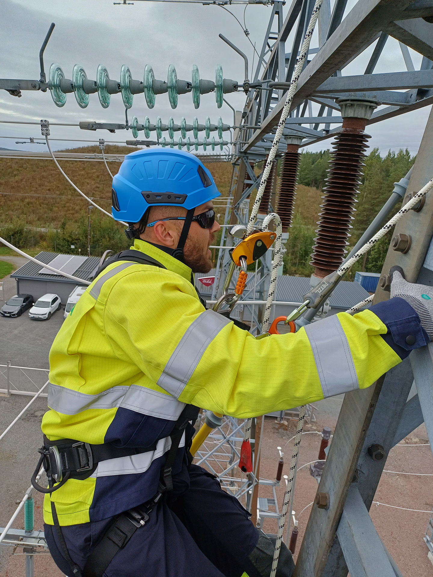 Keltamustaan haalariin ja siniseen kypärään pukeutunut Lauri kiipeilee sähkökentällä.