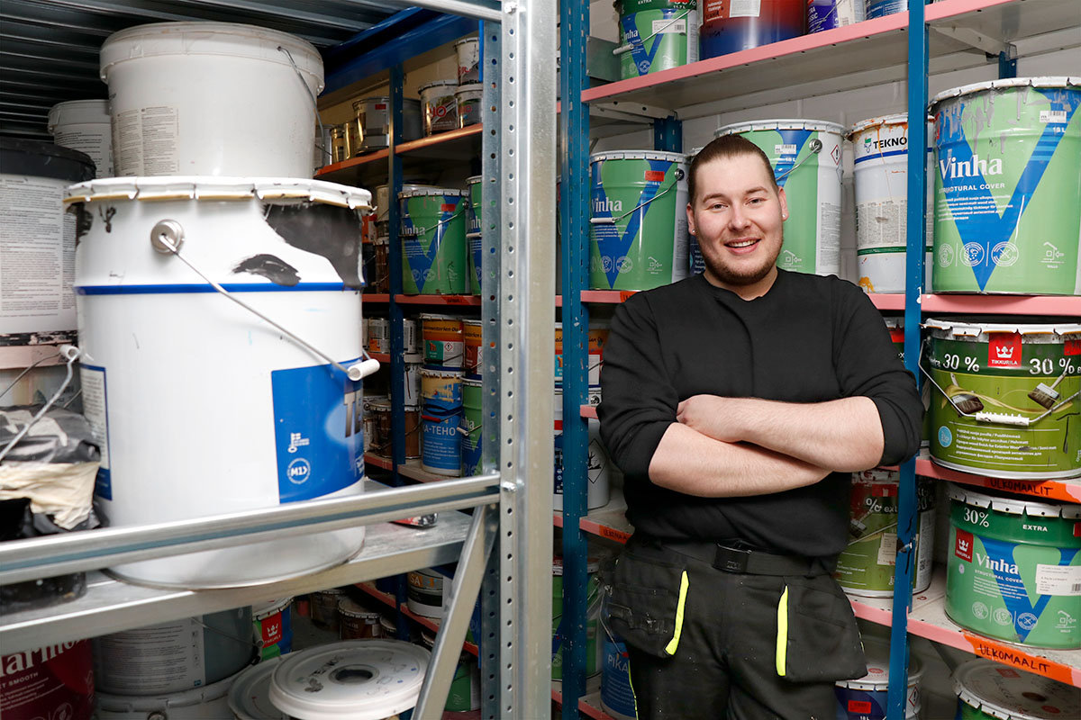 Sisustusalan opiskelija Janne nojaa hyllyyn jossa maalipurkkeja.