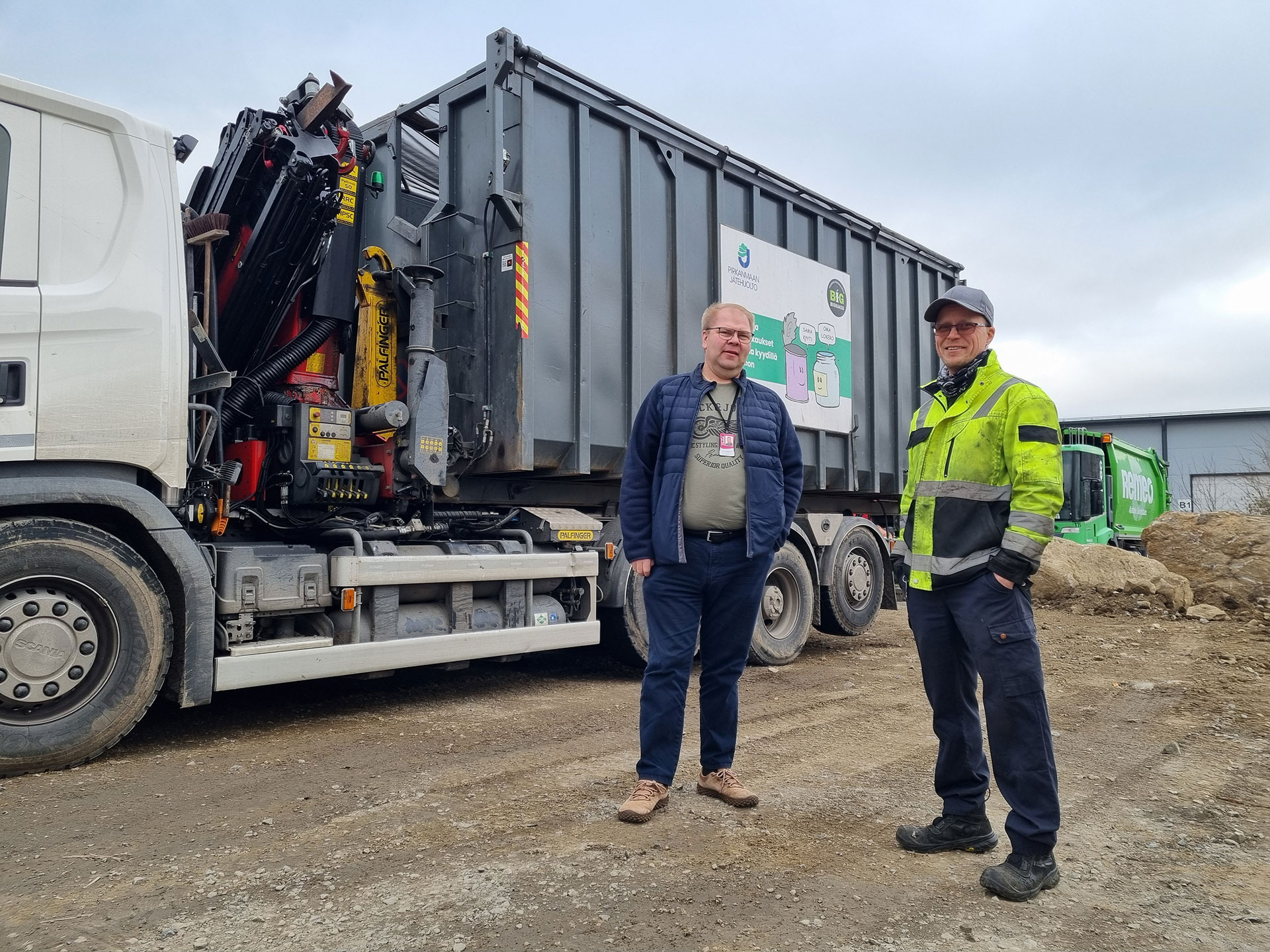 Kouluttaja ja kuljetusalan yrittäjä seisovat jäteauton edessä.